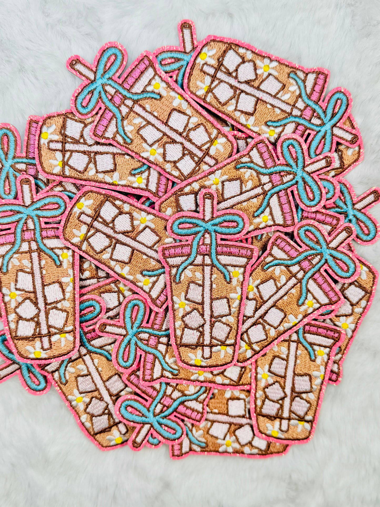 A stack of the Coquette Daisy Iced Coffee Embroidered Patch